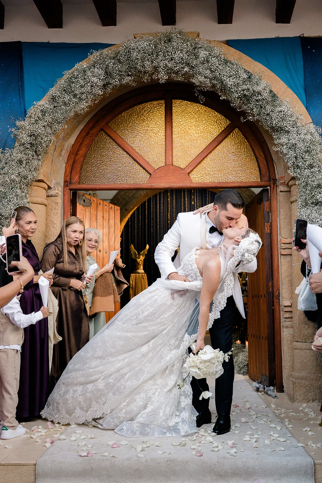 Salida de los novios de la iglesia bajo un arco de flores, fotografiados por Omar Fraija