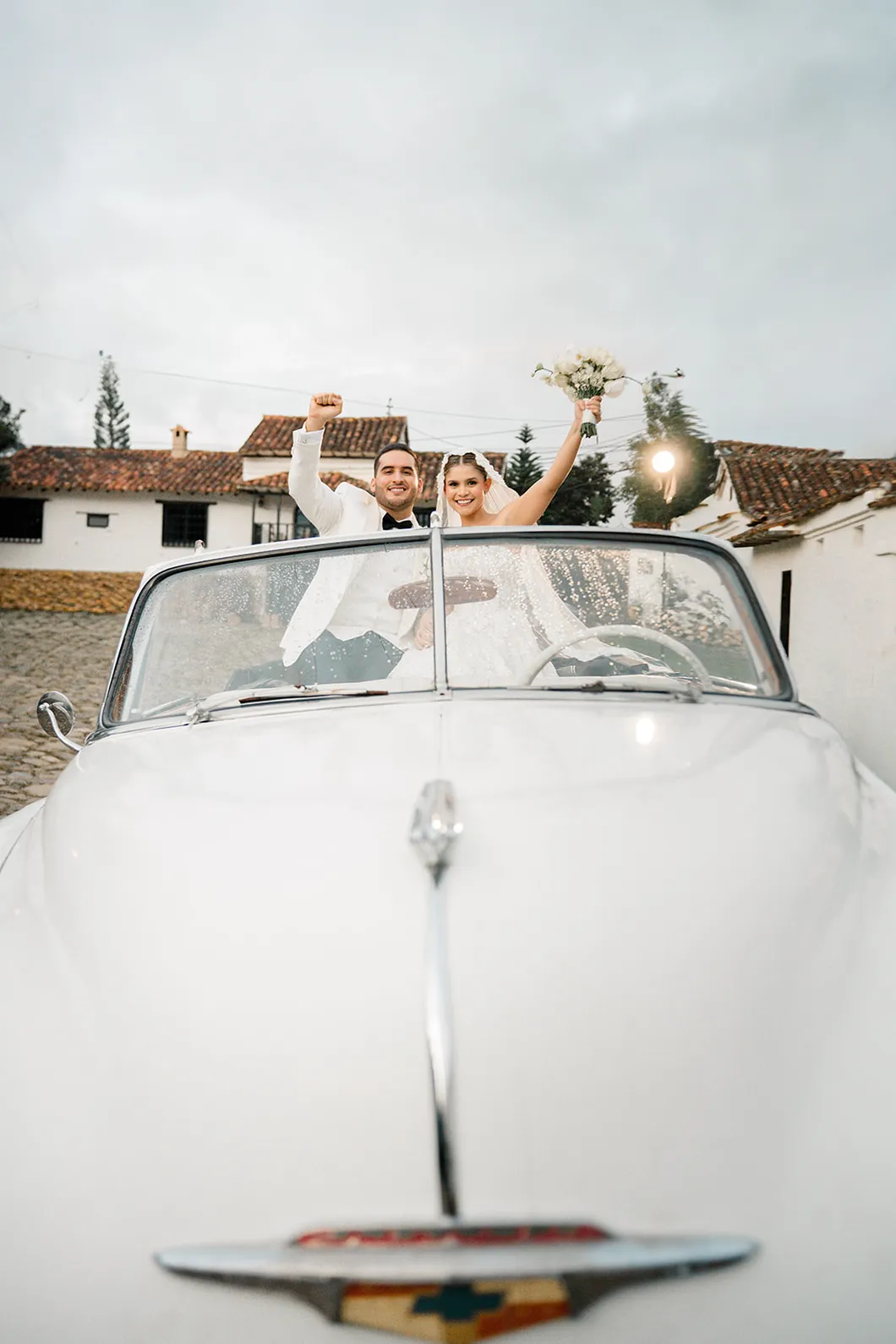 Novios de pie en un carro descapotable blanco, fotografiados por Omar Fraija