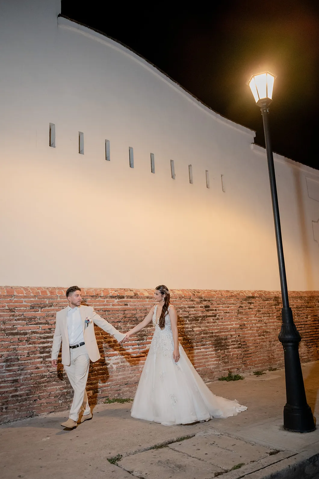 Novios caminando de la mano junto a la muralla de Cartagena de noche, fotografiados por Omar Fraija